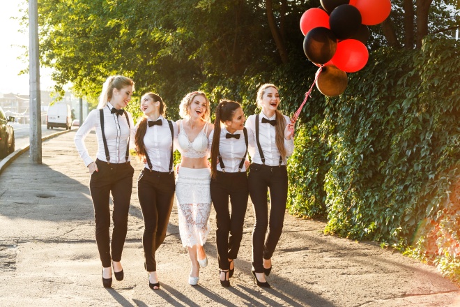 Beautiful happy girls going to celebrate a bachelorette party. Bridesmaids dressed in men's suits. The bride in white sexy dress.